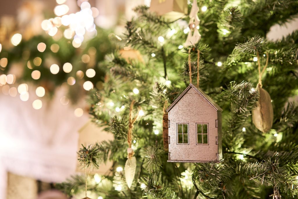 An ornament shaped like a house hangs from a Christmas tree.