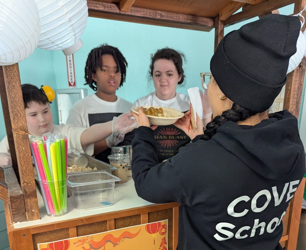 Students serve homemade asian cuisine from a food truck stand in The COVE Schoool dining hall