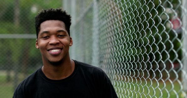 Young adult male smiles while standing near chain link fence