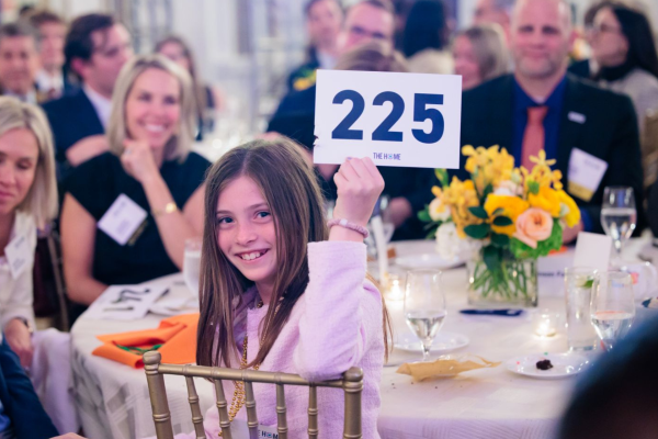 a young girl holds up her family's bid number during the Voices & Visions program