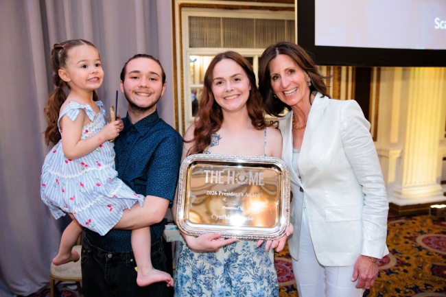 Cynthia Caruso holds the 2026 President's Award with Lesli Suggs. Cynthia is also joined by her brother Aiden who is holding her daughter
